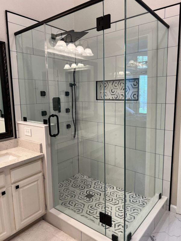 Modern glass shower enclosure with geometric patterned floor tiles.
