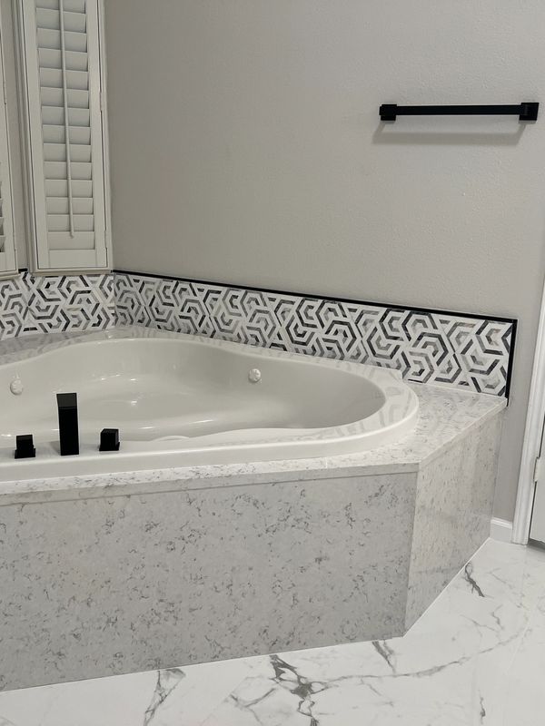 Modern bathroom corner bathtub with geometric tile accents and black fixtures.