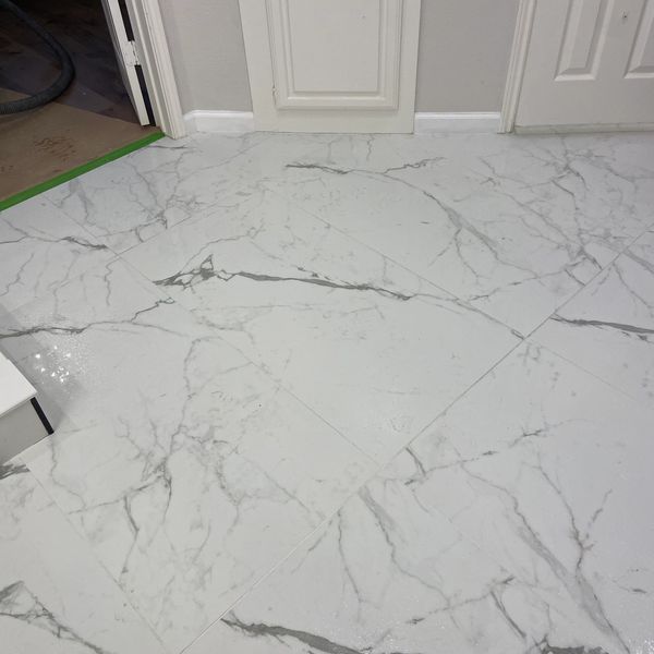 Shiny white marble floor tiles with gray veining near white cabinets and doors.