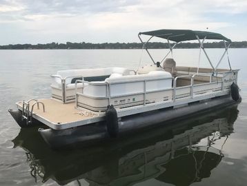 A white pontoon boat floating on calm water with seating and a canopy.