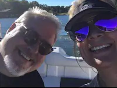 Two people smiling on a boat under a clear sky.