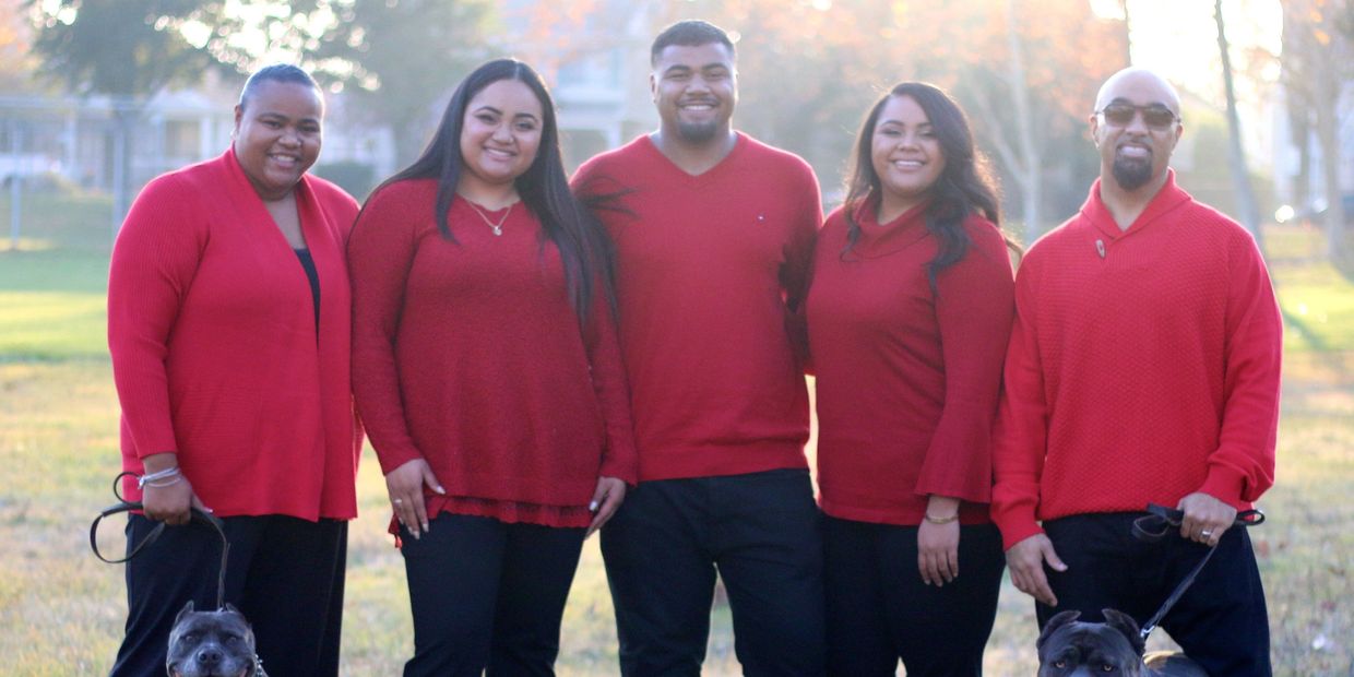 A group of five people in red sweaters posing outdoors with two dogs.