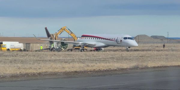 A private jet with a damaged tail being repaired on the ground in an open field.