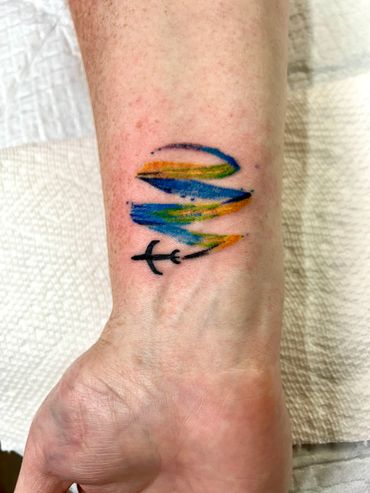 Colorful abstract tattoo with a black arrow on wrist.