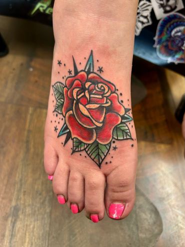 Colorful rose tattoo on foot with bright pink toenails.
