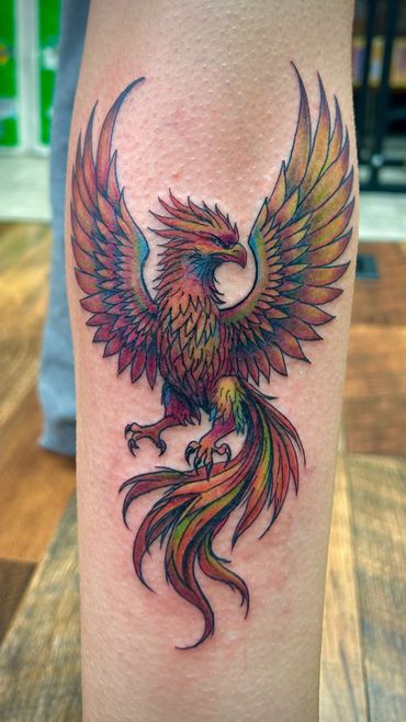 Colorful phoenix tattoo with outstretched wings on forearm.