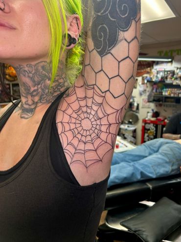 Close-up of a spider web tattoo inside the armpit with hexagonal and cloud tattoos on the arm.