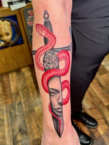 Tattoo of a red snake coiled around a dagger with a face on the blade.