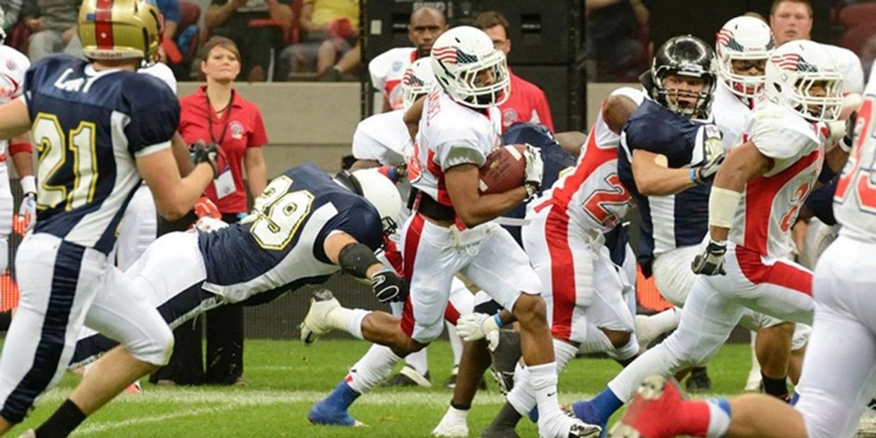 Football player in white runs with the ball while opponents tackle him.