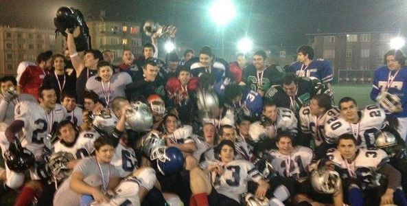 A large group of young football players celebrating on a field at night.
