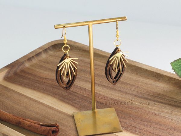 Elegant wooden and gold earrings displayed on a brass stand.