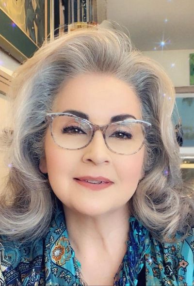 Elegant woman with gray hair and glasses smiling warmly indoors.