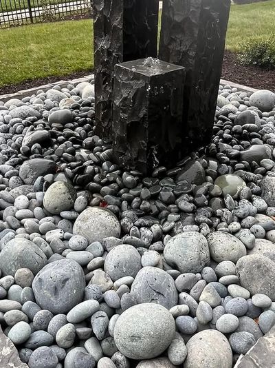Dark textured sculpture surrounded by smooth gray stones in a landscaped garden.