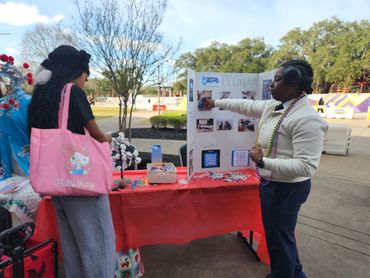 Two women engage at an outdoor informational booth with a colorful display.