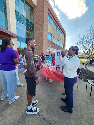 People interacting at an outdoor event near a building on a sunny day.