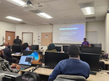 People attending a computer lab session with a presentation on screen.