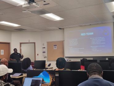 A presenter explains the Red Team concept to an attentive audience in a classroom.
