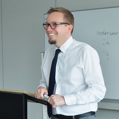 A man in glasses and a tie smiles while standing at a podium.
