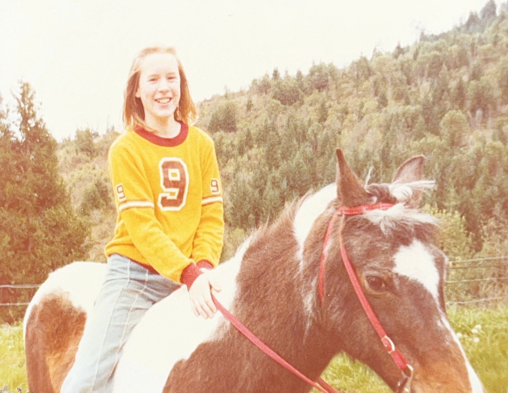 Girl in yellow sweater riding a horse outdoors.