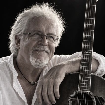 Elderly man smiling with acoustic guitar.