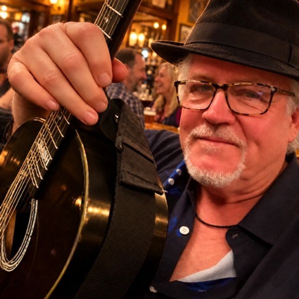 Older man with glasses holding a guitar in a lively bar.