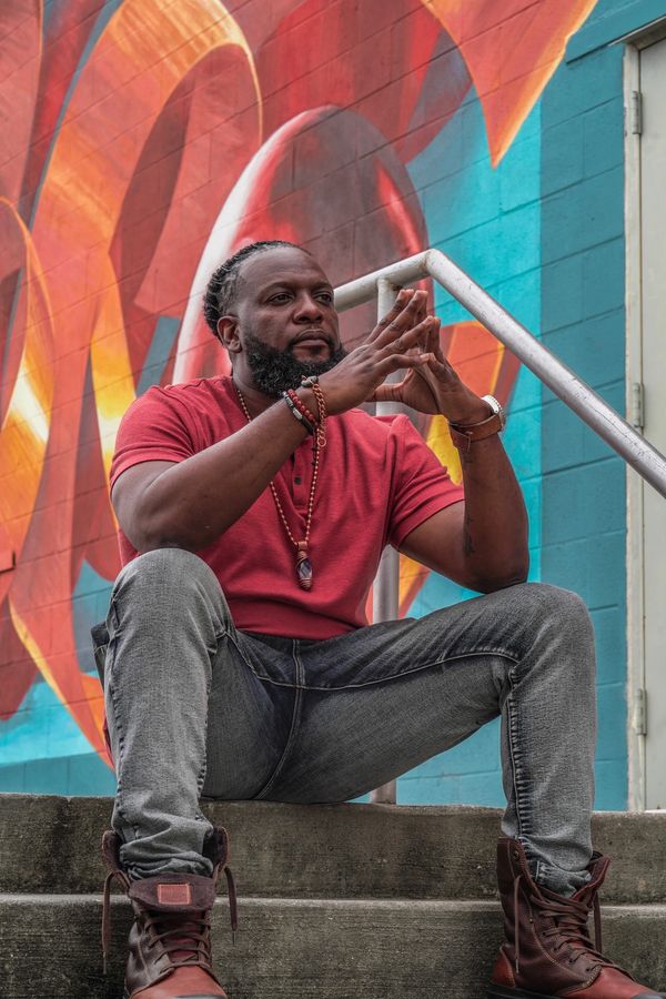 Man in a red shirt sitting on steps against a colorful mural background.