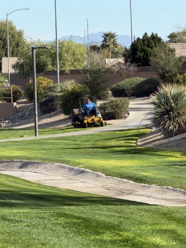 Person mowing grass on a sunny golf course path.
