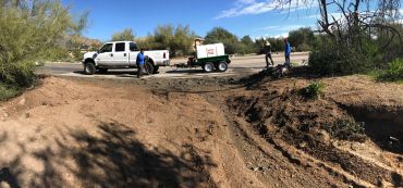 Workers with a truck and equipment in a desert area under a clear sky.