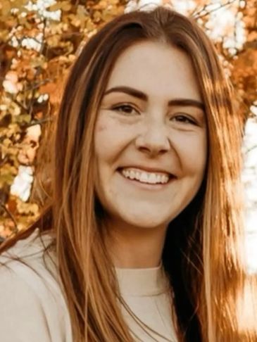Young woman smiling outdoors with autumn leaves in background.