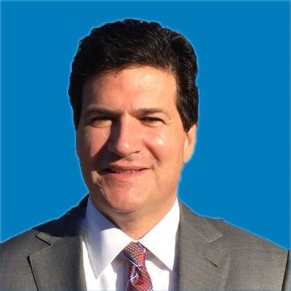 Man in a suit smiling against a blue background.