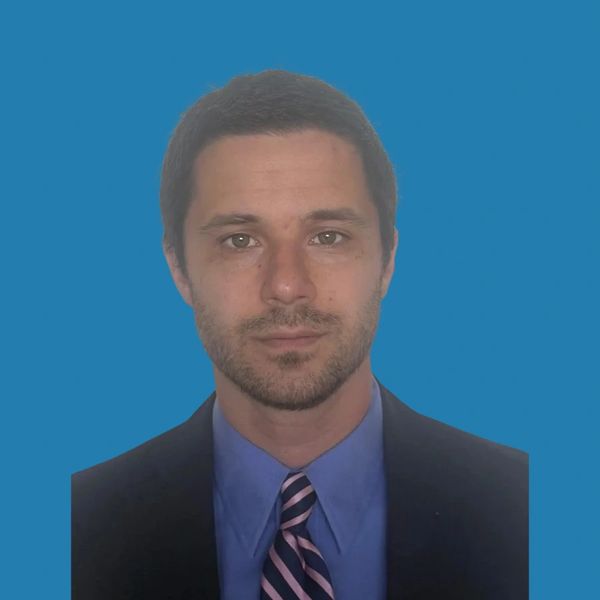 Portrait of a man in formal attire with a blue background.