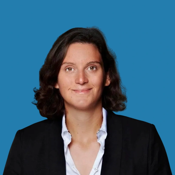 Professional woman with dark hair in suit jacket against blue background.