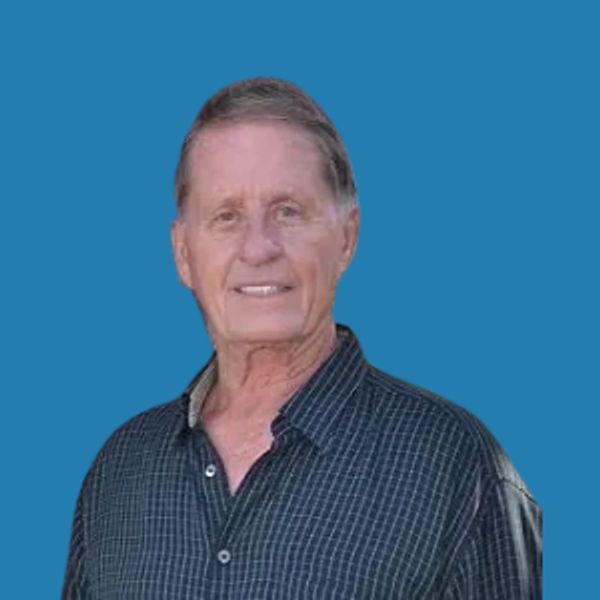 Smiling elderly man in a checkered shirt with blue background.
