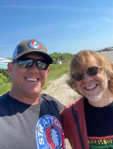 Two smiling men wearing sunglasses outdoors on a sunny day.