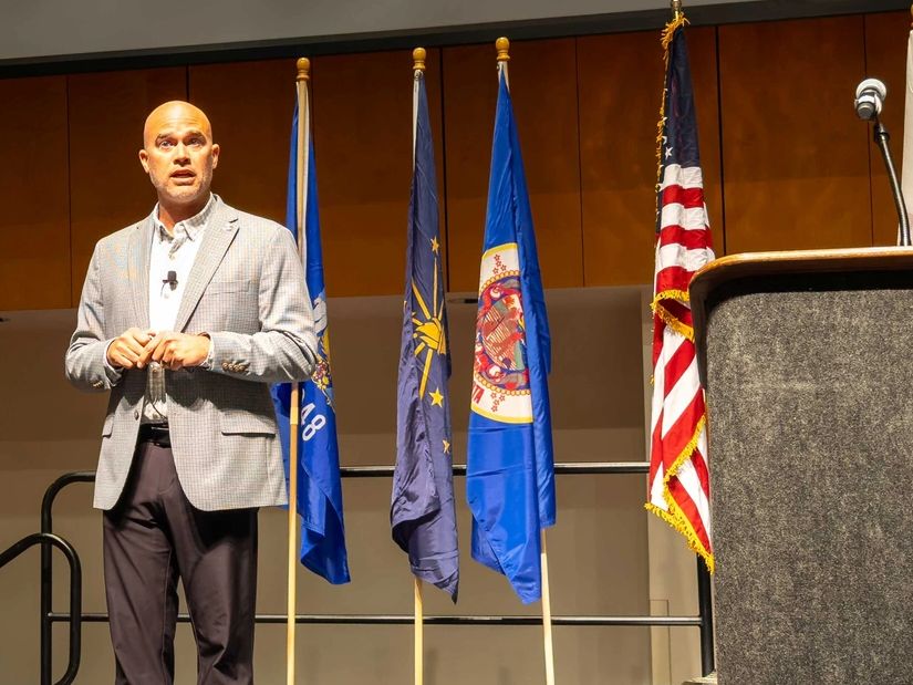 Man delivering a presentation on stage with a large screen behind him.