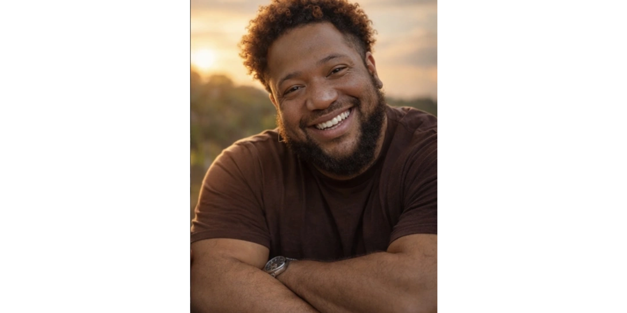 Smiling man with curly hair and beard outdoors at sunset.