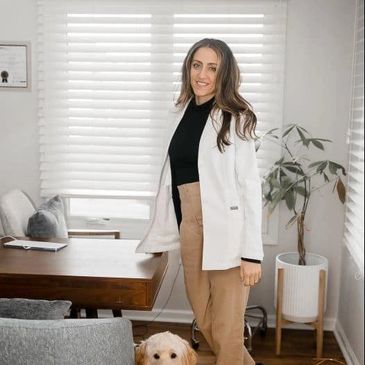 A woman smiling indoors with a dog by her side in a cozy room.