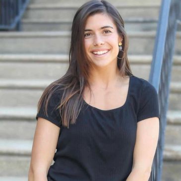 Smiling woman with long hair sitting on stairs, wearing a black top.