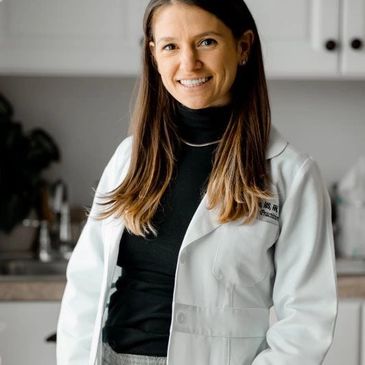 Smiling female doctor in a white coat standing in a kitchen.
