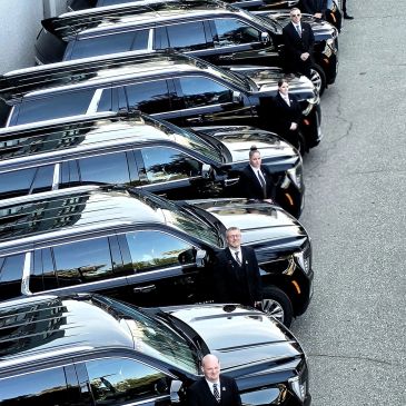 Line of black SUVs with security personnel standing beside them.