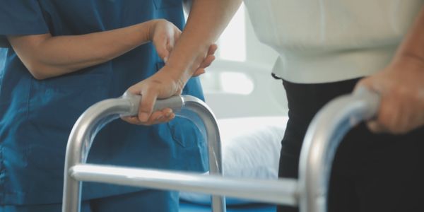 Nurse assists elderly person with walker.