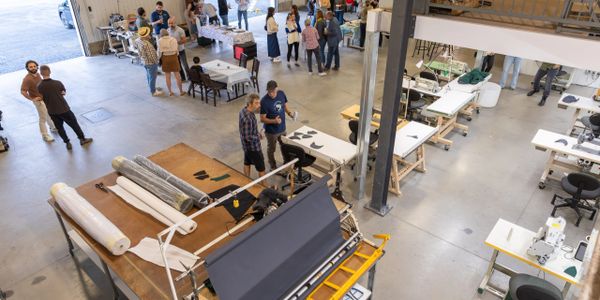 People socializing in a large, well-lit workshop with tables and equipment.