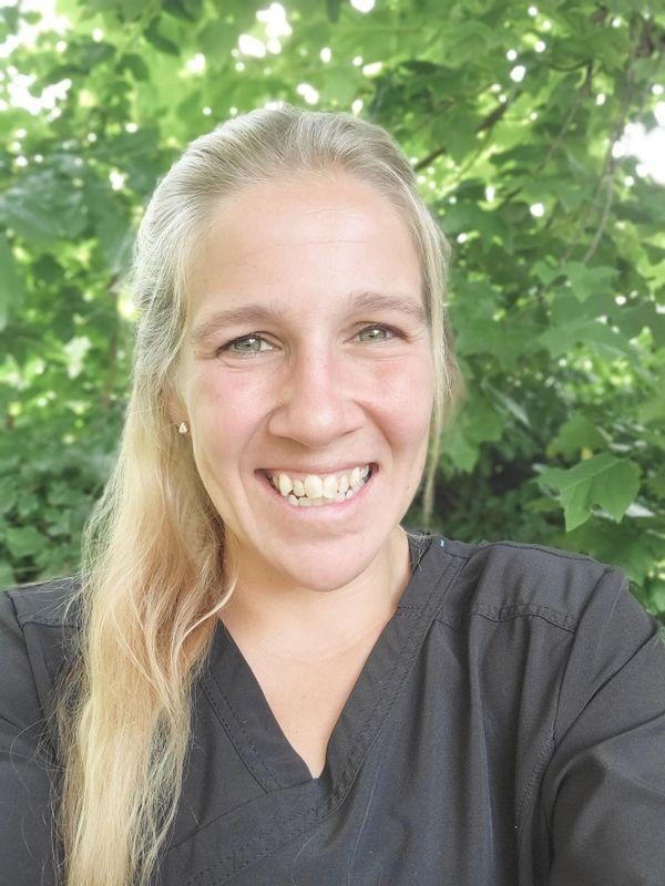 Smiling woman in black scrubs with green leafy background.