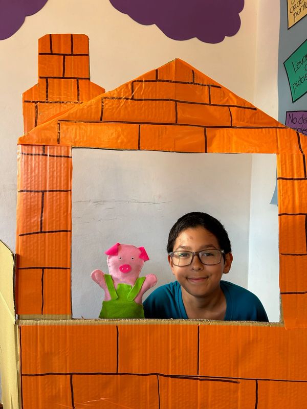 Boy with a pig puppet in a cardboard puppet theater.