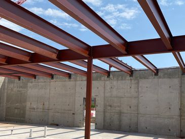 Steel beams and concrete walls under a blue sky at a construction site.