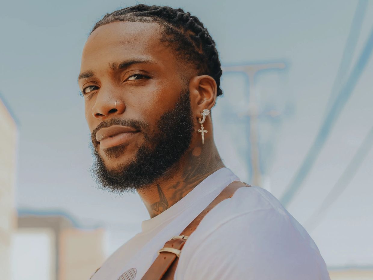 Confident man with braided hair, beard, and stylish jewelry.