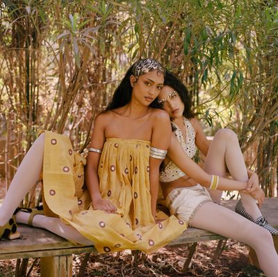 Two women in bohemian-style outfits sitting on a bench under greenery.