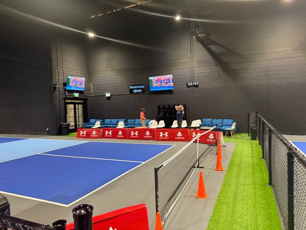 Indoor tennis court with seating and digital screens on the wall.