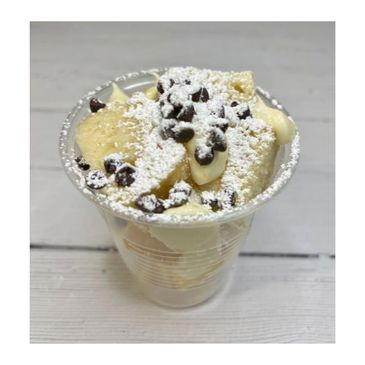 Dessert cup with cake pieces, cream, chocolate chips, and powdered sugar.