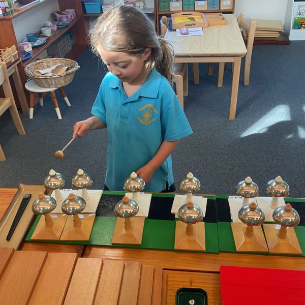 Young girl playing with musical bells in a classroom.